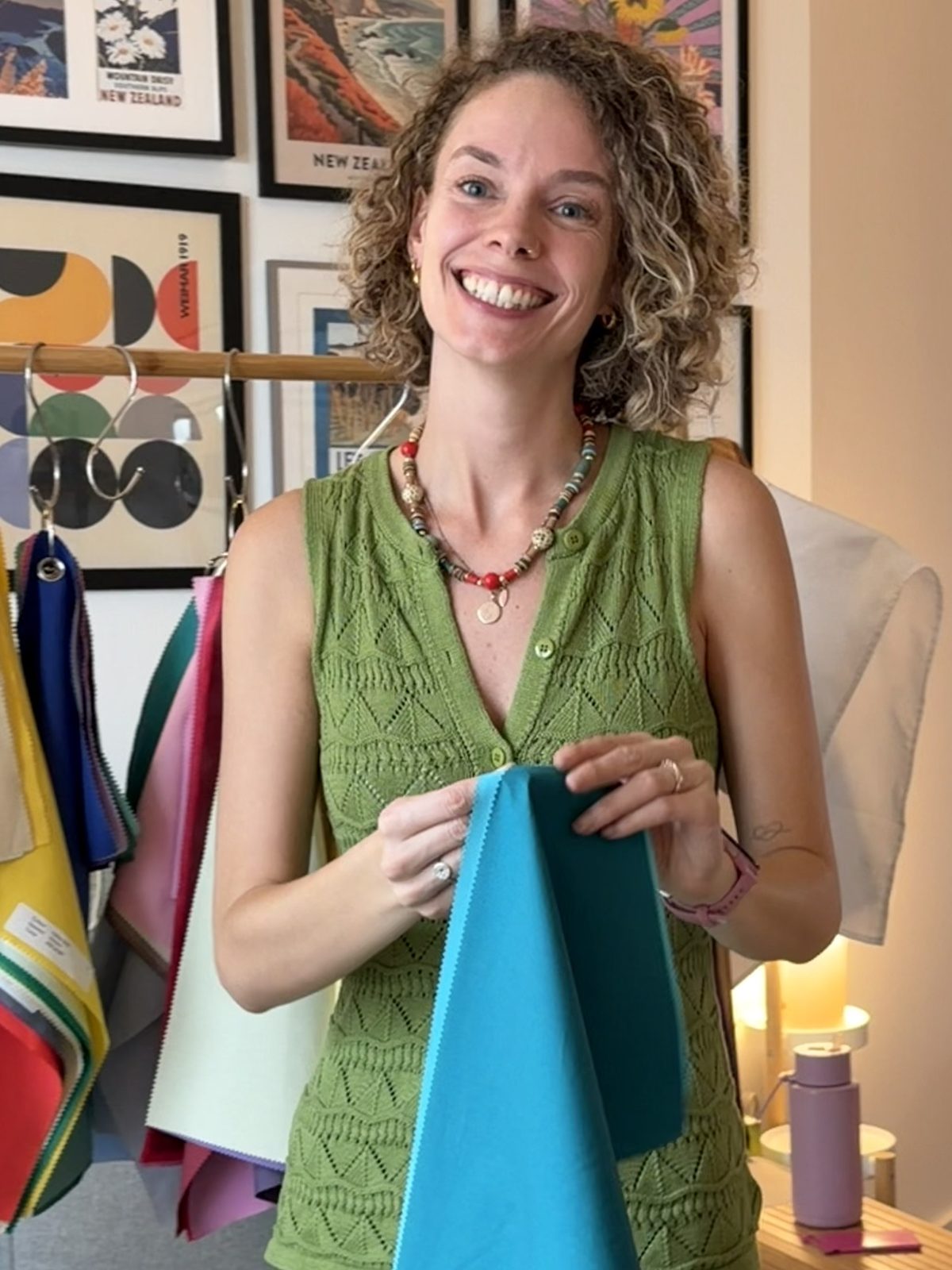 Shann smiling, holding a bright blue drape, her rail of colours behind her