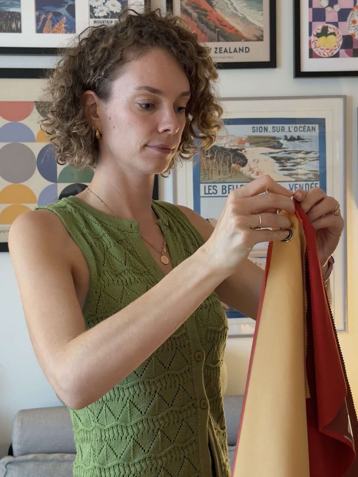 Shann holding a red drape beside a warmer yellow one, watching closely to see which one suits better