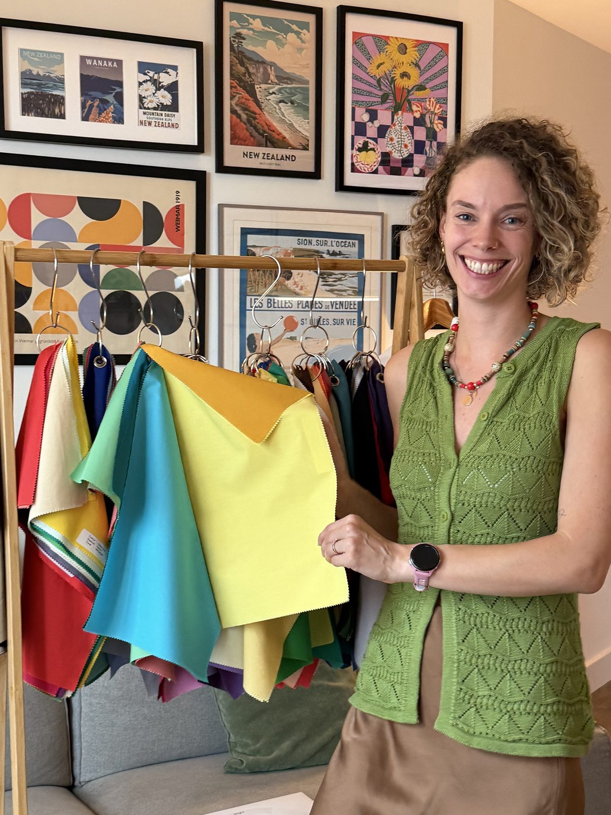 Shann smiling beside her rail of precision-dyed drapes, holding a yellow and a gold one up to the light