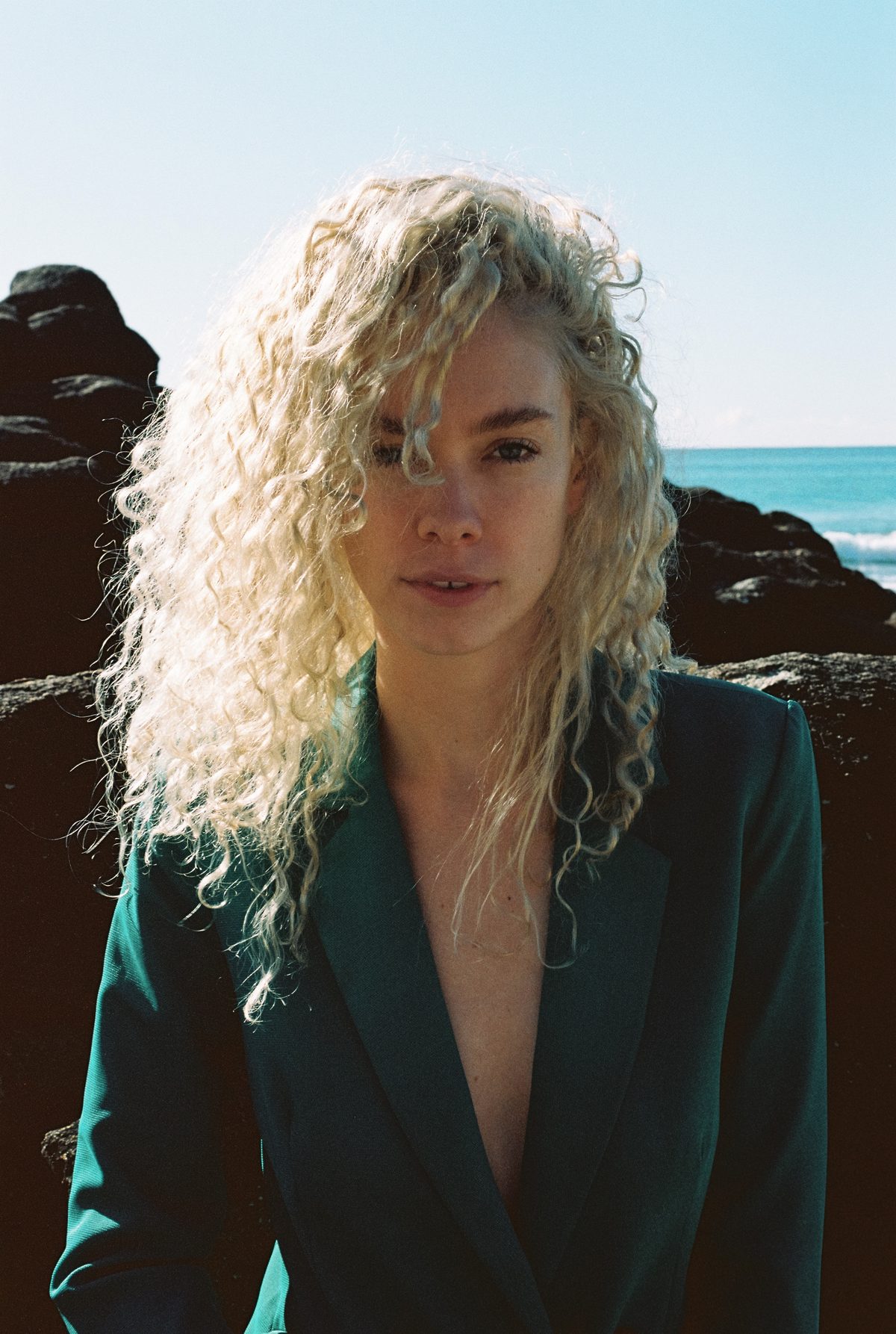 Shann photographed on the rocks by the sea in a deep teal jacket, from her modelling career